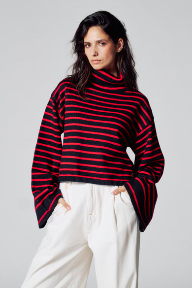 Sweat-shirt multicolore avec col montant de Le Fabuleux Marcel de Bruxelles, à rayures horizontales rouges et noires, associé à un pantalon blanc.
