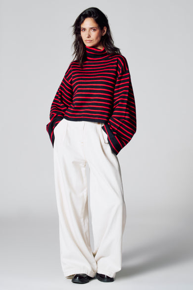 Manteau multicolore de Le Fabuleux Marcel de Bruxelles, avec des rayures rouges et noires, combiné à un pantalon blanc.