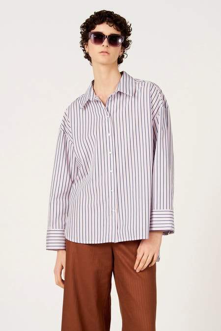 Veelkleurig hemd met lange mouwen van Le Fabuleux Marcel de Bruxelles, met een gestreept patroon, gedragen met bruine broek en zonnebril.
