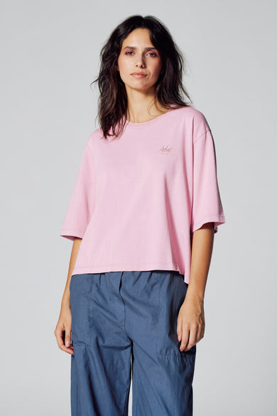 T-shirt rose à manches courtes de Le Fabuleux Marcel de Bruxelles, porté avec un pantalon bleu.