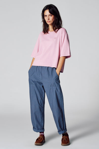 T-shirt rose à manches courtes de Le Fabuleux Marcel de Bruxelles, porté avec un pantalon bleu et des chaussures marrons.