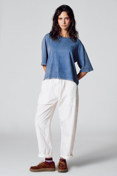 T-shirt bleu à manches courtes de Le Fabuleux Marcel de Bruxelles, porté avec un pantalon blanc et des chaussures marrons.