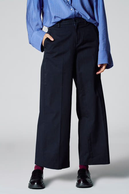 Blauwe chino van Le Fabuleux Marcel de Bruxelles, met wijde pijpen en losse pasvorm, gecombineerd met een blauw gestreept overhemd.
