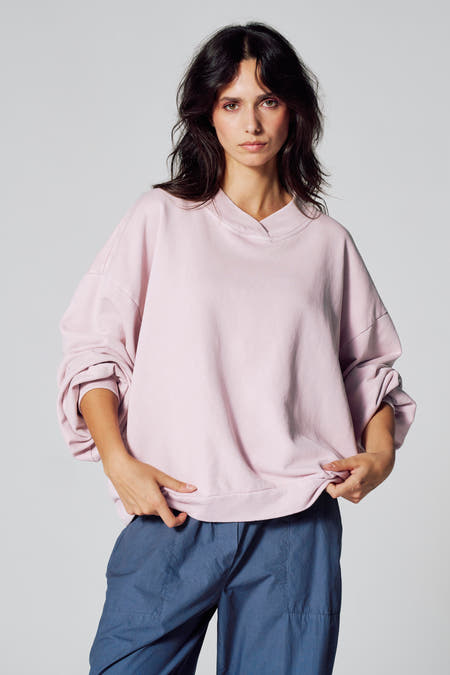 Roze sweater van Le Fabuleux Marcel de Bruxelles, met lange mouwen en blauwe broek.
