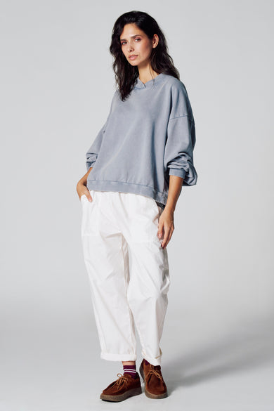 Sweat-shirt bleu de Le Fabuleux Marcel de Bruxelles, à manches longues, associé à un pantalon blanc et des chaussures marrons.