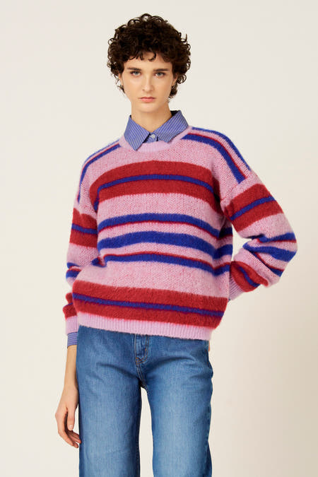 Multikleurige trui van Le Fabuleux Marcel de Bruxelles, met horizontale strepen in roze, rood en blauw, gedragen over een blauw gestreept overhemd met jeans.
