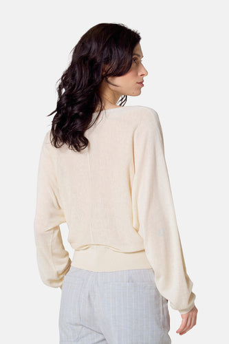 Vrouw met bruin haar, ivoorkleurige trui en blauw gestreepte broek, zij aanzicht.
