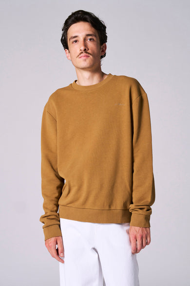Sweater ocre avec col rond de Le Fabuleux Marcel de Bruxelles, porté avec un pantalon blanc.