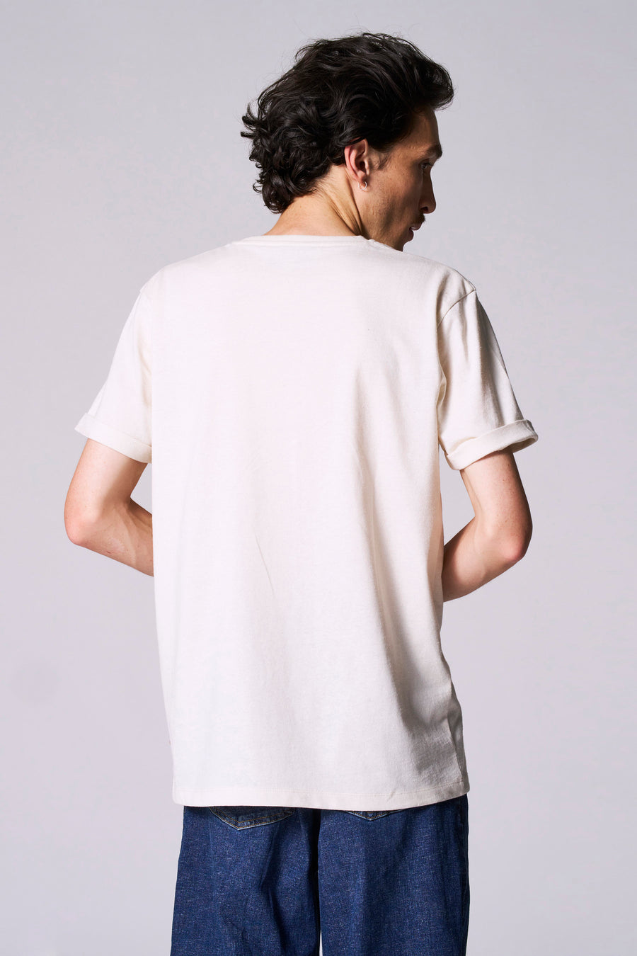 Man van achteren, crème T-shirt, blauwe jeans.