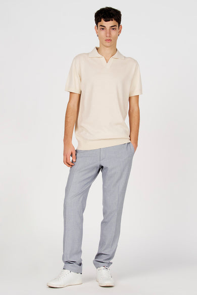Witte polo van Le Fabuleux Marcel de Bruxelles, met korte mouwen, gedragen met een grijze pantalon en witte sneakers.

