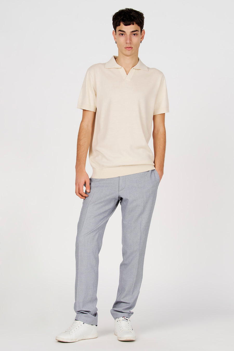 Polo blanche de Le Fabuleux Marcel de Bruxelles, à manches courtes, portée avec un pantalon gris et des baskets blanches.