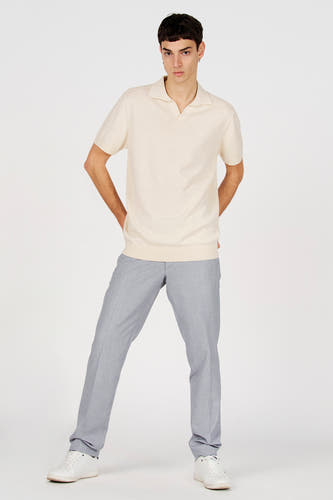 Polo blanche de Le Fabuleux Marcel de Bruxelles, à manches courtes et portée avec un pantalon gris et des baskets blanches.