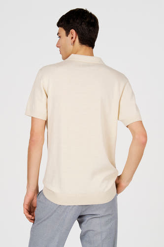 Polo blanche de Le Fabuleux Marcel de Bruxelles, vue de dos, portée avec un pantalon gris.