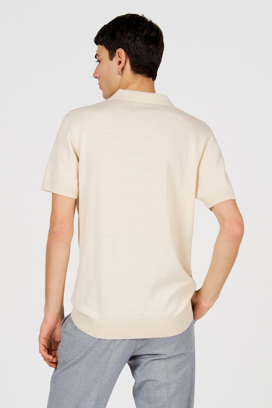 Polo blanche de Le Fabuleux Marcel de Bruxelles, vue de dos, portée avec un pantalon gris.