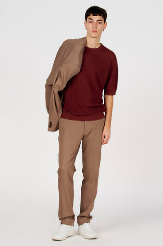 T-shirt marron (manches courtes) de Le Fabuleux Marcel de Bruxelles, porté avec un pantalon marron et une veste sur l'épaule.