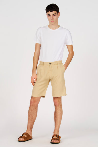 Bermuda beige de Le Fabuleux Marcel de Bruxelles, porté avec un t-shirt blanc et des sandales marron.