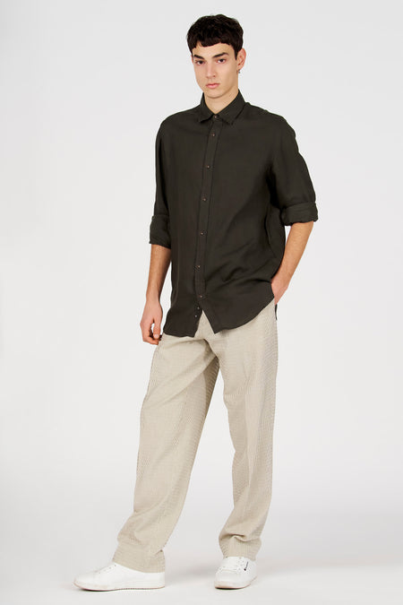 Chemise vert foncé de Le Fabuleux Marcel de Bruxelles avec manches retroussées et boutons marron, portée avec un pantalon beige à rayures.