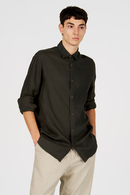 Chemise en lin vert foncé de Le Fabuleux Marcel de Bruxelles avec manches retroussées et boutons foncés, portée avec un pantalon rayé.