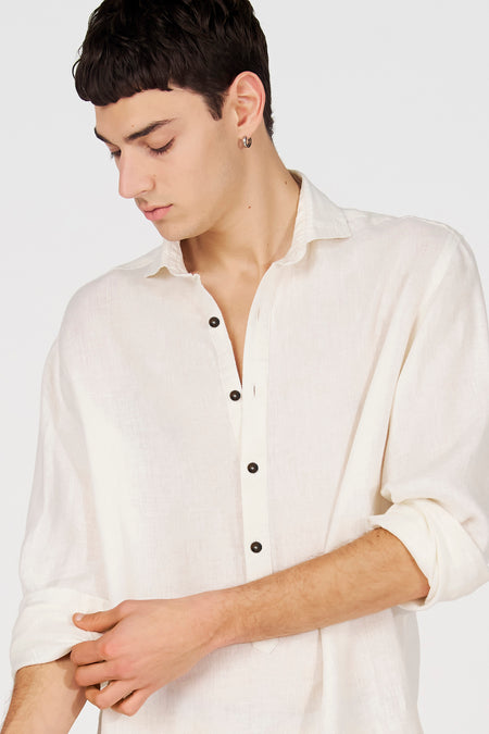 Chemise en lin blanc à manches longues de Le Fabuleux Marcel de Bruxelles, avec boutons foncés, manche retroussée.