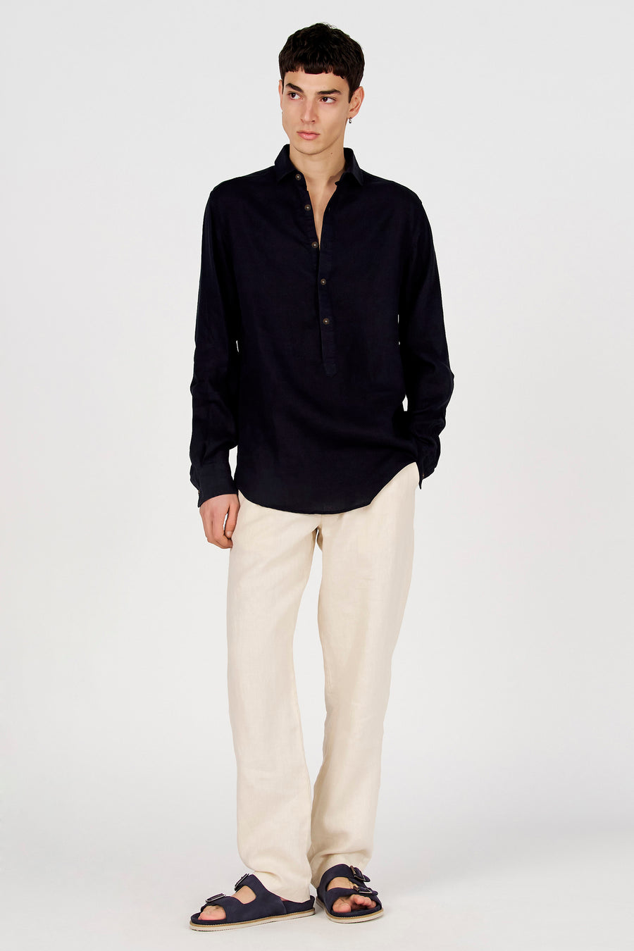 Donkerblauw overhemd met lange mouwen van Le Fabuleux Marcel de Bruxelles, met Henley-hals en knopen, gedragen met beige broek en sandalen.