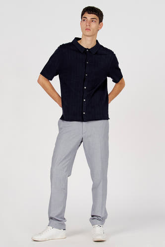 Polo bleu de Le Fabuleux Marcel de Bruxelles, à manches courtes et patte boutonnée, combiné avec un pantalon gris et des baskets blanches.