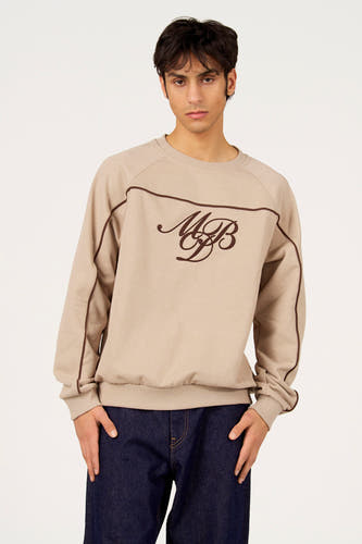Pull gris à col rond de Le Fabuleux Marcel de Bruxelles, avec des accents marron et des initiales brodées. Porté avec un jean foncé.