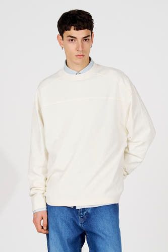 Witte sweater met ronde hals van Le Fabuleux Marcel de Bruxelles, gedragen over een lichtblauw overhemd en met blauwe jeans.
