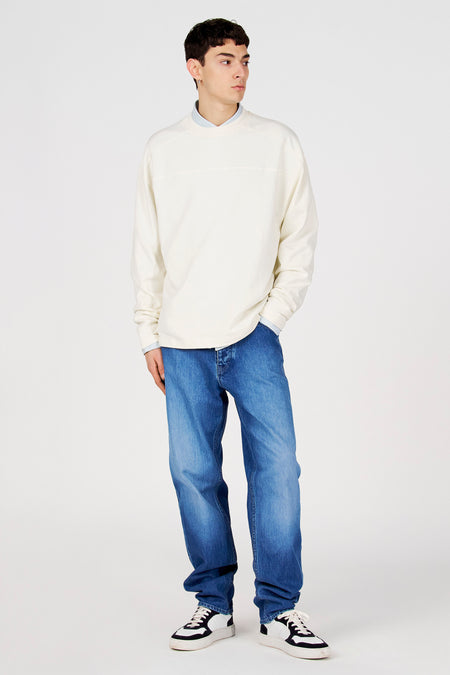 Pull blanc de Le Fabuleux Marcel de Bruxelles, porté avec une chemise bleu clair et un jean bleu.