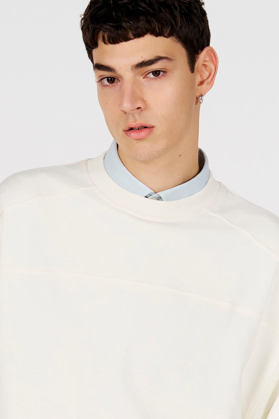 Witte sweater van Le Fabuleux Marcel de Bruxelles, met een subtiele, horizontale band op de borst en een lichtblauwe blouse eronder.
