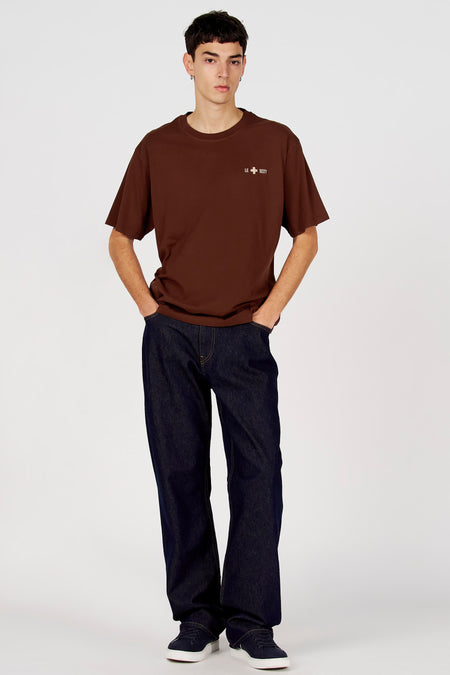 T-shirt marron à manches courtes de Le Fabuleux Marcel de Bruxelles, porté avec un jean bleu foncé et des baskets bleues.
