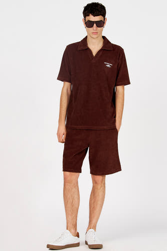 Bruine polo van Le Fabuleux Marcel de Bruxelles met korte mouwen en een logo, gedragen met een bijpassende short en witte sneakers.
