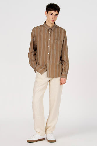 Chemise marron (manches longues) de Le Fabuleux Marcel de Bruxelles, à rayures blanches, portée avec un pantalon crème et des baskets blanches.