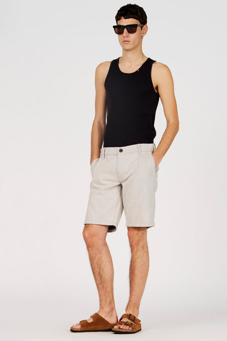 Ecru short van Le Fabuleux Marcel de Bruxelles, met insteekzakken en bruine sandalen.
