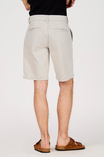 Ecru short van Le Fabuleux Marcel de Bruxelles, met een subtiele textuur en bruine sandalen.
