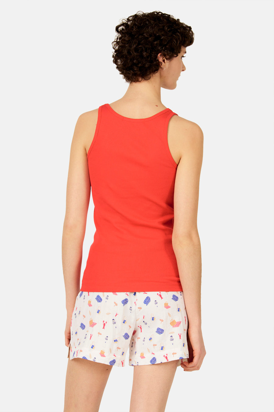 Rood geribbelde singlet van Le Fabuleux Marcel de Bruxelles, rugzicht op vrouw met korte, krullende haren en geprinte shorts.