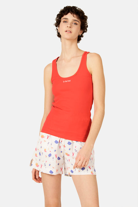 Débardeur côtelé rouge de Le Fabuleux Marcel de Bruxelles avec le texte 'le bel été', porté avec un short blanc à motifs de plage.