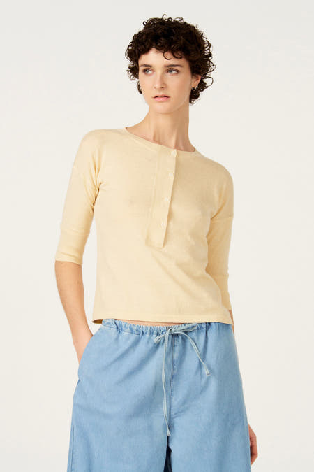 Ecru trui met ronde hals van Le Fabuleux Marcel de Bruxelles, met korte knoopsluiting en gedragen met een lichtblauwe broek.
