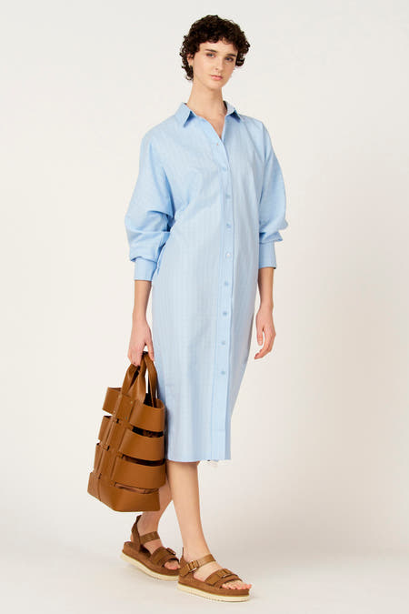 Blauw kleedje met lange mouwen van Le Fabuleux Marcel de Bruxelles, met knoopsluiting en gedragen met bruine sandalen en een tas.
