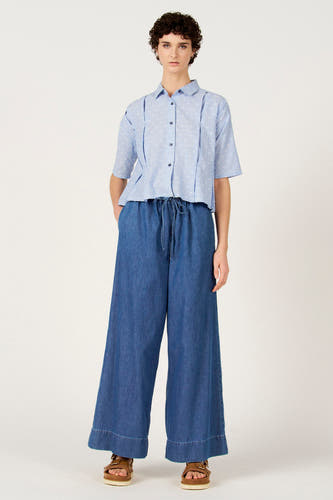 Blauw gestreept overhemd met korte mouwen van Le Fabuleux Marcel de Bruxelles, met witte stippen en gedragen met wijde, donkerblauwe broek.
