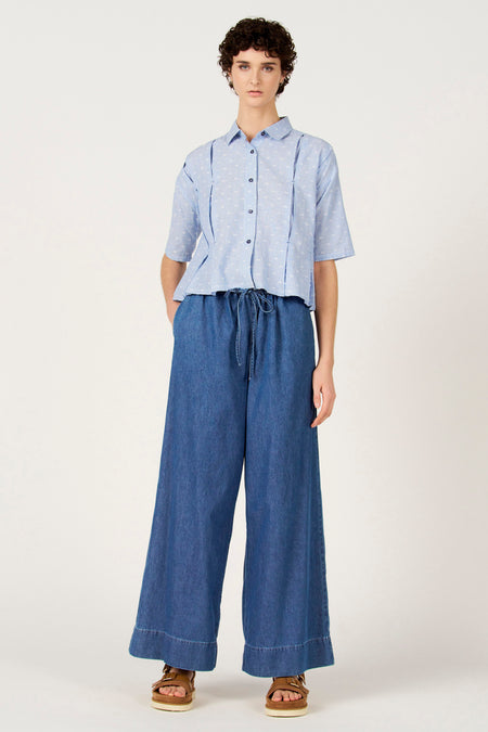 Blauw gestreept overhemd met korte mouwen van Le Fabuleux Marcel de Bruxelles, met witte stippen en gedragen met wijde, donkerblauwe broek.
