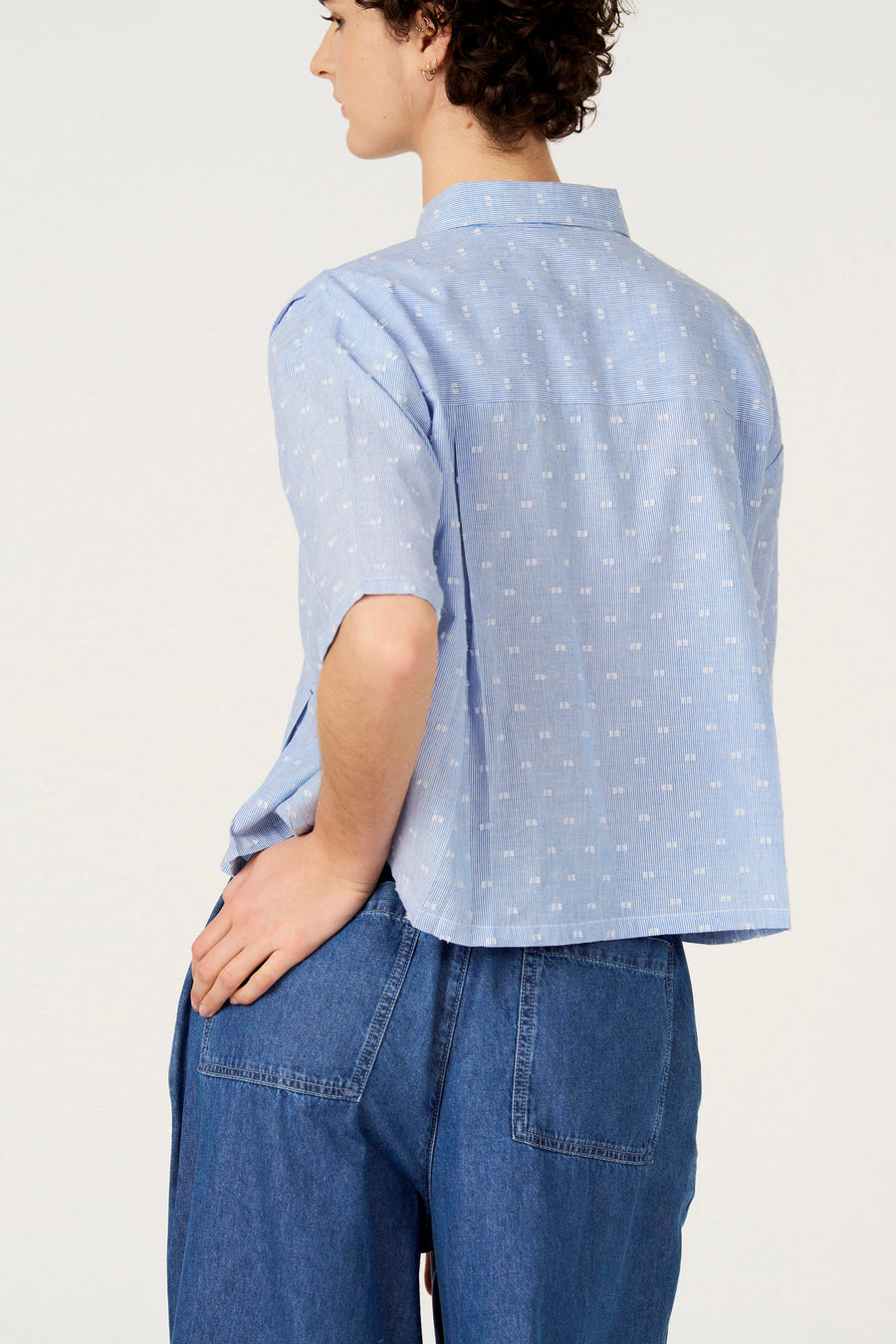 Blauw gestreept overhemd met korte mouwen van Le Fabuleux Marcel de Bruxelles, met witte stippen en losvallende jeans.
