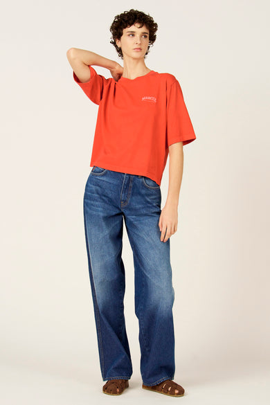 Rood T-shirt met korte mouwen van Le Fabuleux Marcel de Bruxelles, gedragen met wijde jeans en sandalen.
