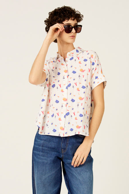 Multikleurig hemd met korte mouwen van Le Fabuleux Marcel de Bruxelles, met strandthema en gedragen met een donkerblauwe jeans.
