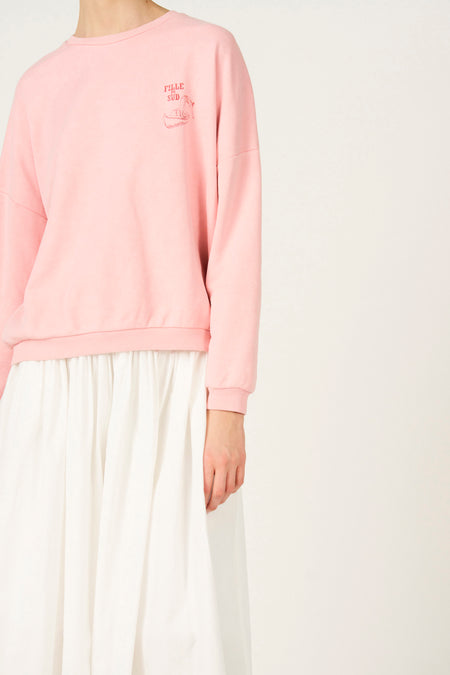 Roze sweater van Le Fabuleux Marcel de Bruxelles, met kleine rode print en gecombineerd met een witte rok.
