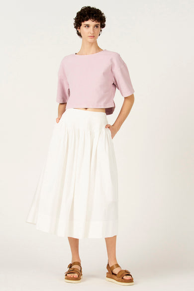 Jupe blanche de Le Fabuleux Marcel de Bruxelles, portée avec un crop top rose et des sandales marron.
