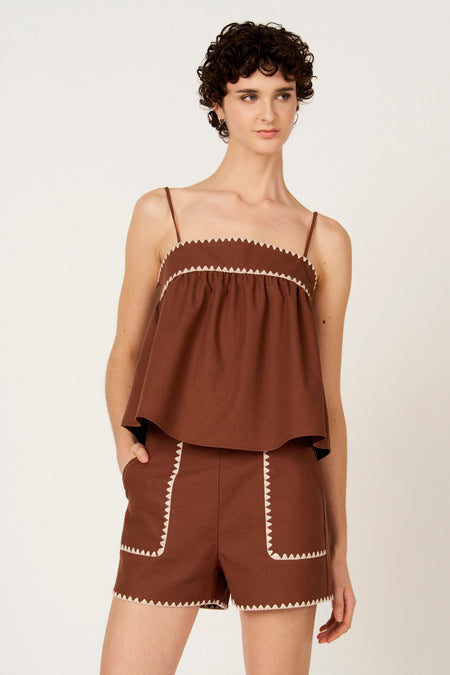 Bruine mouwloze blouse van Le Fabuleux Marcel de Bruxelles met witte zigzag rand, gedragen met bijpassende shorts.
