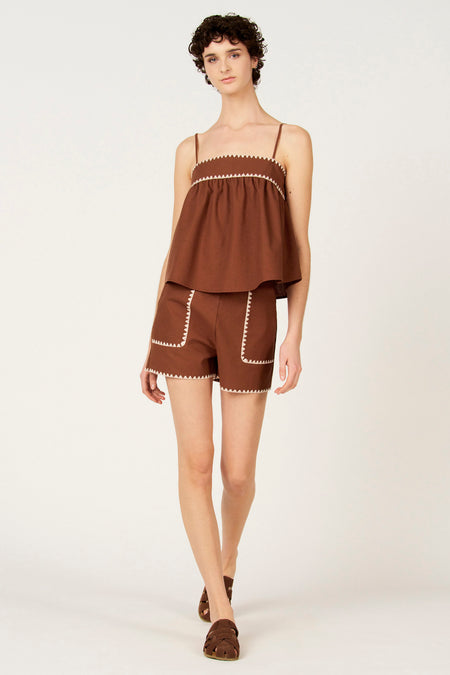 Mouloze bruine blouse van Le Fabuleux Marcel de Bruxelles, met witte zigzagdetails langs de halslijn, gecombineerd met bruine shorts en sandalen.
