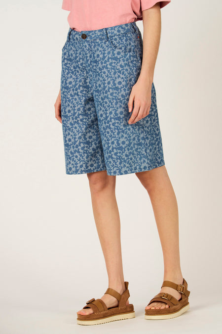Blauwe bermuda van denim, van Le Fabuleux Marcel de Bruxelles, met bloemmotief, gecombineerd met bruine sandalen en een roze T-shirt.