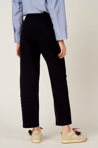Pantalon bleu de Le Fabuleux Marcel de Bruxelles, vu de dos, combiné avec une chemise rayée et des baskets crème.