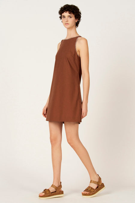 Bruine kleedje zonder mouwen van Le Fabuleux Marcel de Bruxelles, met witte zigzagstiksels langs de armsgaten en halslijn, gedragen met bruine sandalen.